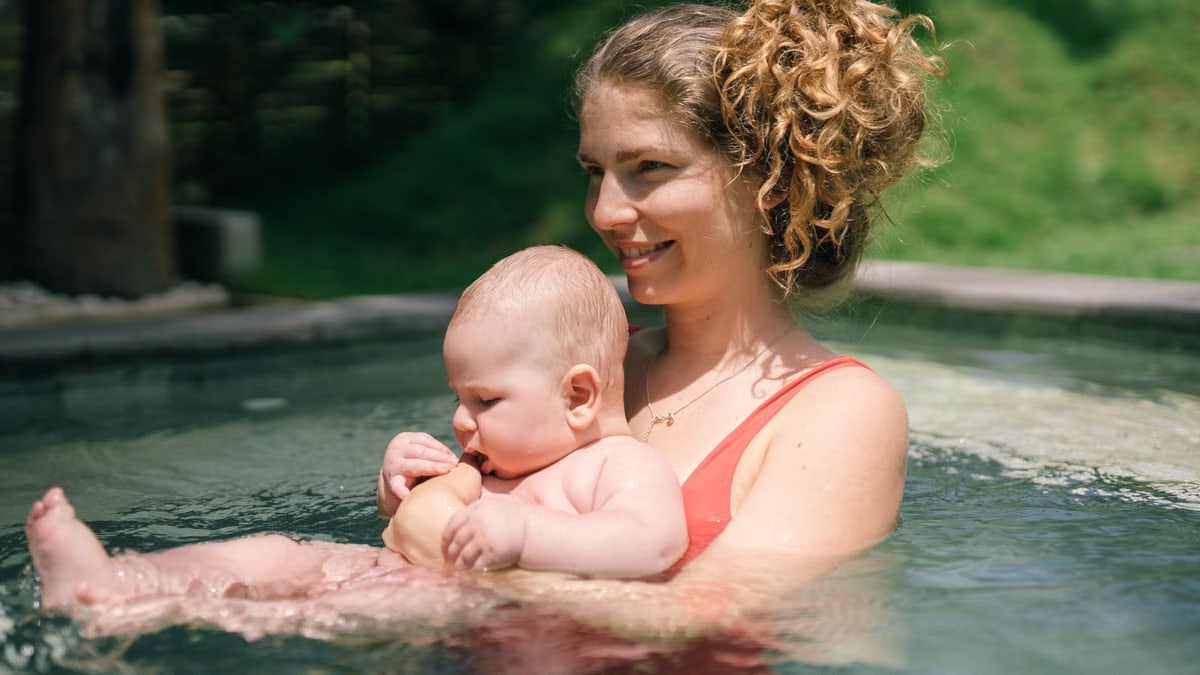 A mother joyfully holds her baby while swimming together in an outdoor pool.